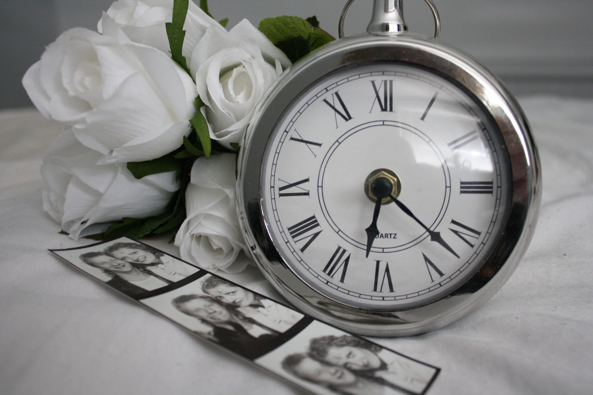 Eine Uhr angelehnt an weiße Rosen aus Siegen mit Bilder im Vordergrund